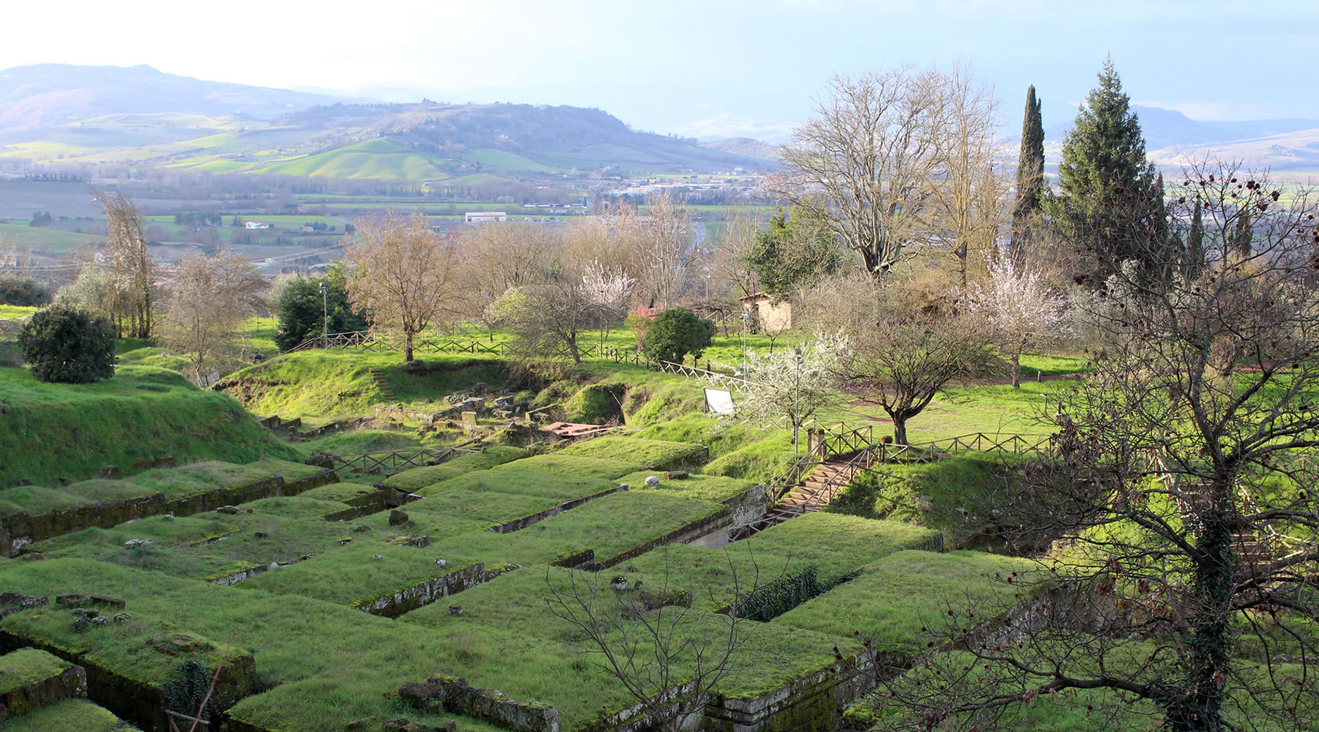 Vue aérienne de la nécropole étrusque avec des tombes à tumulus recouvertes d’un toit herbeux, entourée de collines.