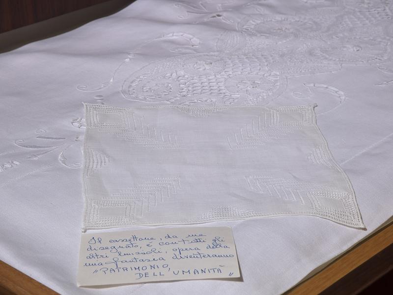 Lenzuolo ricamato a mano con fazzoletto esposti in una vetrina del Museo della Canapa, insieme a un biglietto scritto a mano
