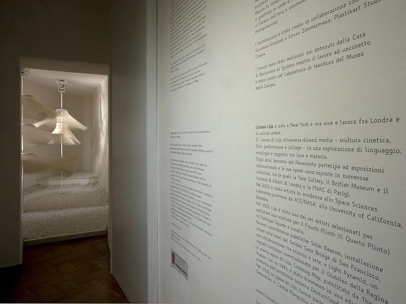 Pannelli informativi con scritte nere su muro bianco inerenti all’installazione artistica che si intravede in secondo piano