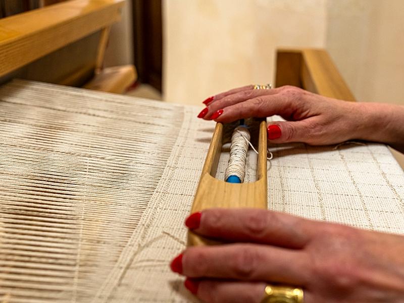Mani al lavoro su un telaio manuale che realizzano un tessuto con filato di cotone e canapa.