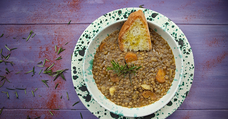 Lentil soup with carrots and potatoes, rosemary and a slice of toasted bread on a decorated plate, top view.