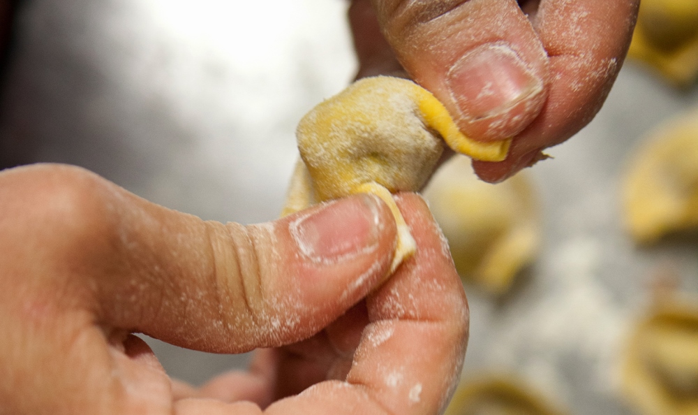 Artisanal preparation of a cappelletto, with hands shaping and sealing fresh pasta around the filling.