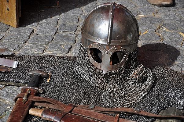 Medieval helmet and chainmail resting on stone paving, with sword and leather belt
