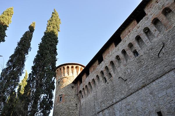 Walls and tower of the Knights of Malta Castle in Magione, surrounded by cypress trees under a clear sky