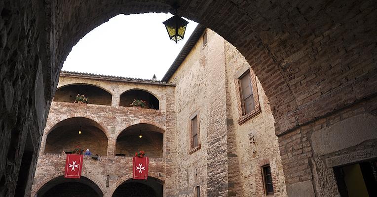 Inner courtyard of the Knights of Malta Castle in Magione, with brick arches and banners bearing the eight-pointed cross