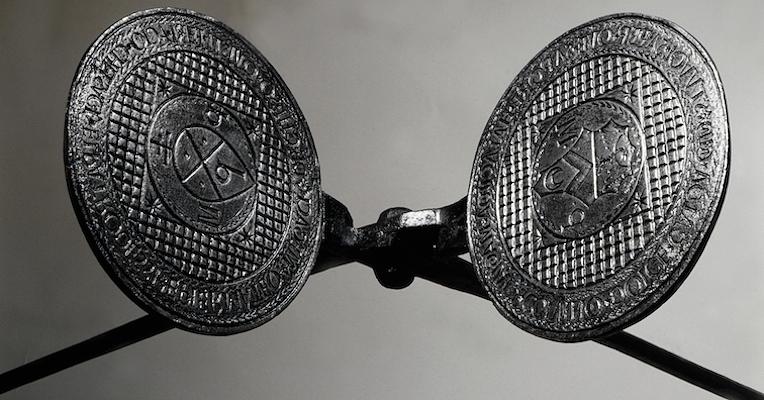 Close-up of a wafer iron with engraved plates and coats of arms, on a neutral background.