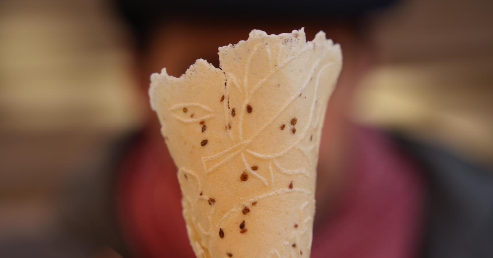 Thin wafer with leaf patterns and small anise seeds, shown in close-up against a blurred background.