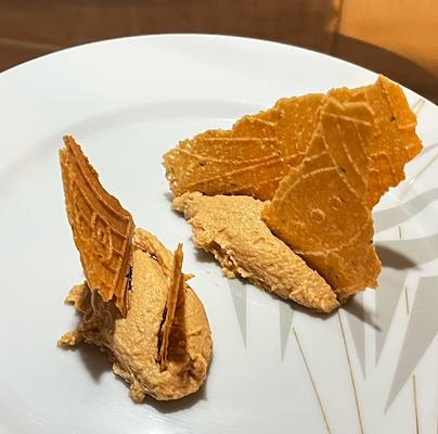 Ice cream on a white plate topped with broken, crunchy wafers.