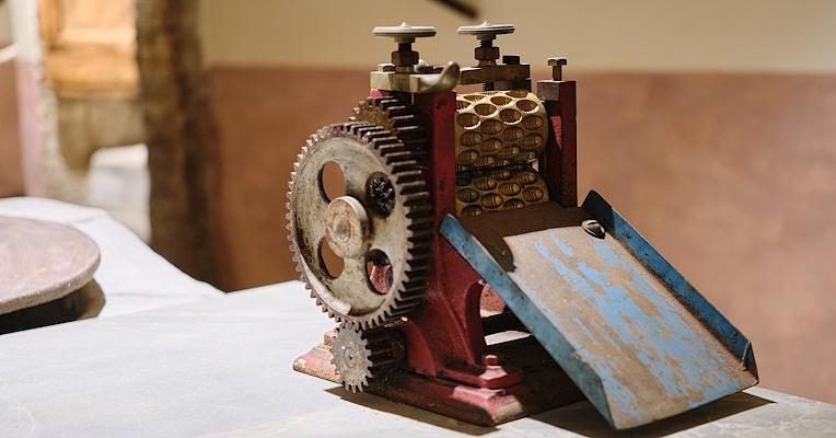 Antique machine with gears and rollers, used for chocolate processing, displayed on a laboratory bench.
