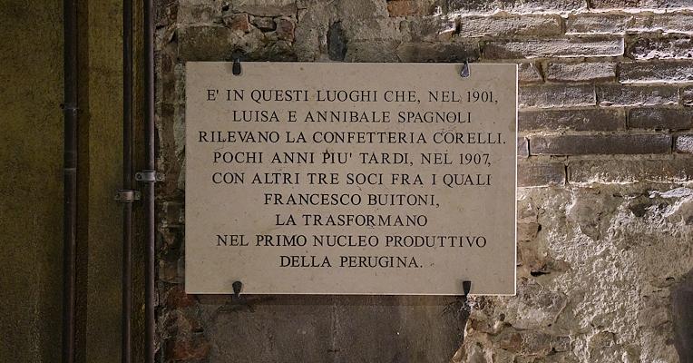 Stone commemorative plaque on a brick wall recounting the founding of Perugina in the early 20th century.