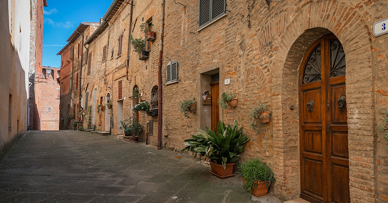 Vicolo in mattoni nel centro storico di Città della Pieve, con porte in legno e vasi di piante lungo la via.