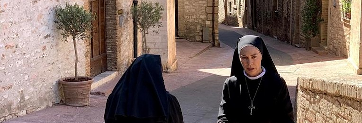 Elena Sofia Ricci, nei panni di Suor Angela, con un'altra suora in un vicolo medievale soleggiato di Assisi.