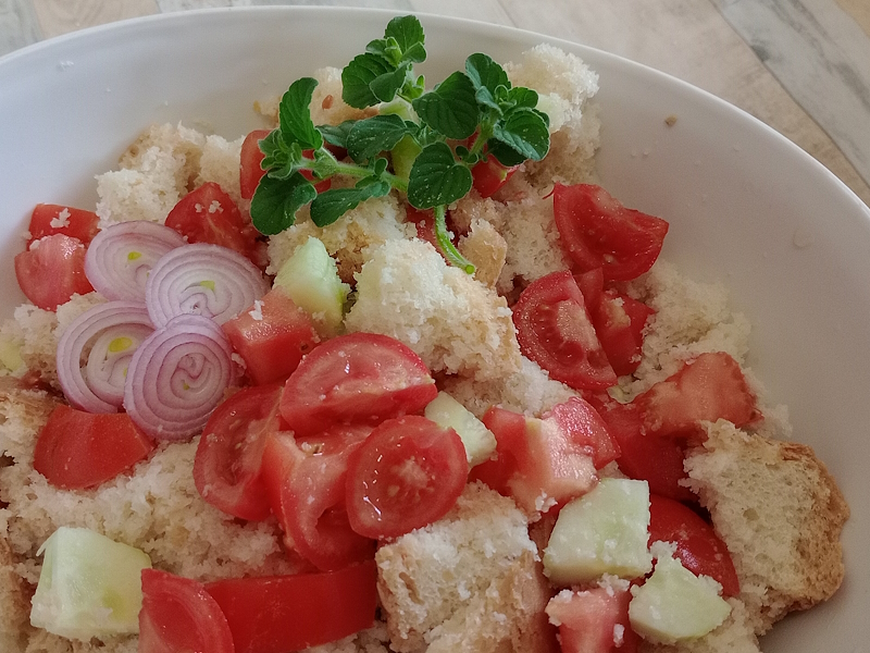 A white bowl of panzanella dressed with cherry tomatoes, cucumber and sliced onion, garnished with fresh mint.