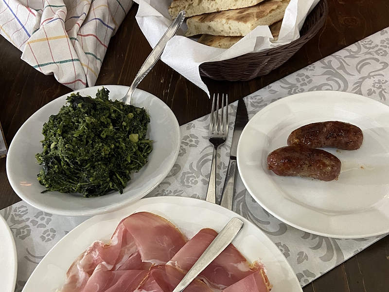 Plate with prosciutto, sausage, greens and torta al testo on a rustic table