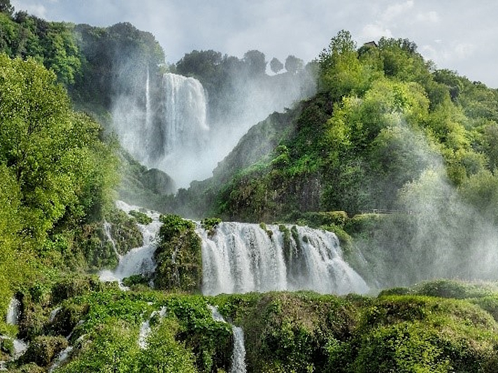 View of the Marmore Waterfalls with multiple cascades flowing among vegetation and rocks.