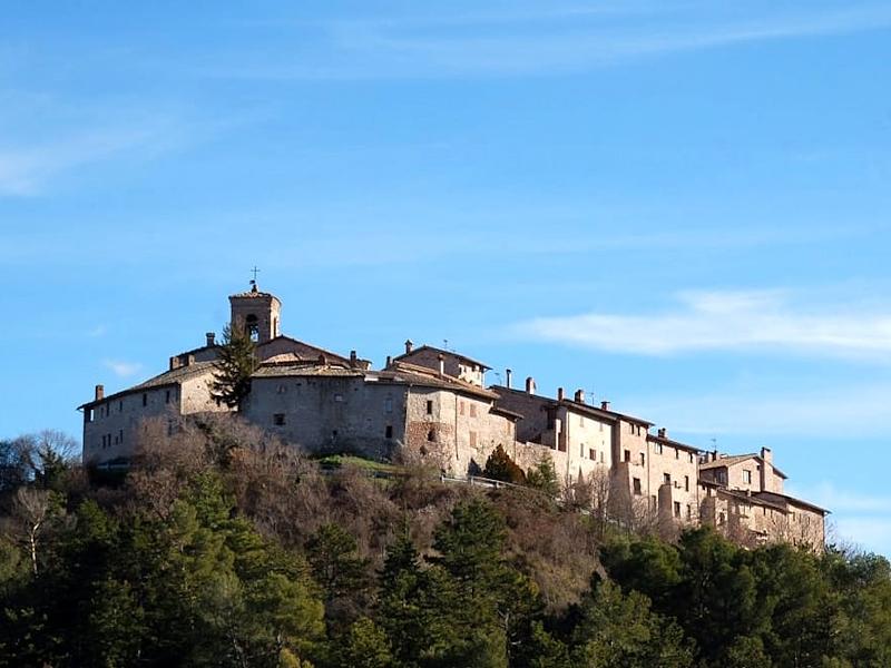 Vue d'en bas du château médiéval de Macerino, situé sur une colline au cœur des bois des Monts Martani, avec un ciel clair en arrière-plan
