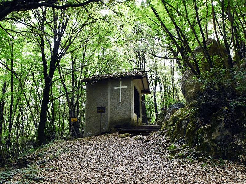 Piccola cappella dello Speco francescano immersa nel bosco, con una croce bianca sulla facciata laterale.