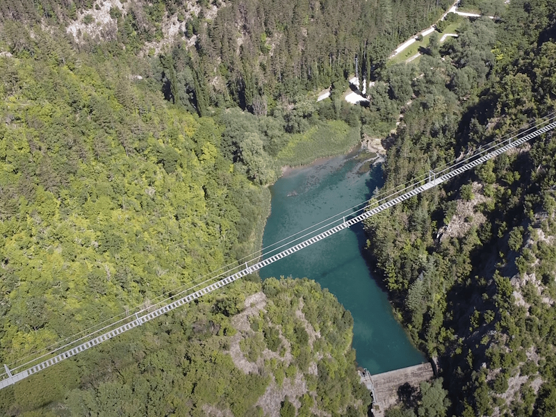 Vista aerea del Ponte Tibetano di Sellano sospeso sopra la valle del fiume Vigi, tra boschi e pareti rocciose della Valnerina.