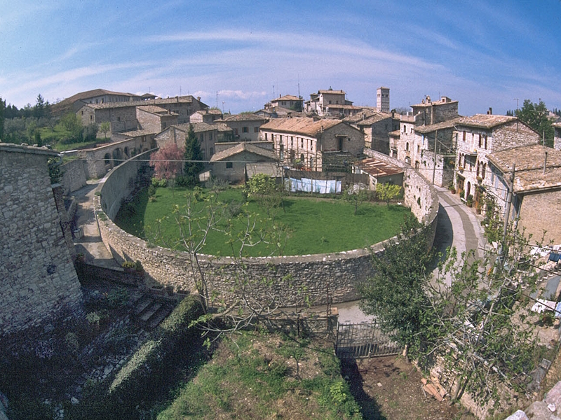 Aerial view of the Roman Amphitheatre district of Assisi, where the elliptical outline of the ancient arena is still visible among the houses.