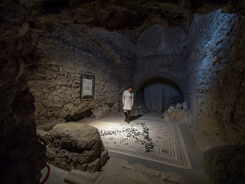 Visitor observing a mosaic floor inside the Roman House of Spoleto, surrounded by ancient stone walls and column bases.