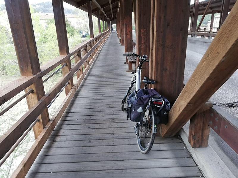 Covered wooden footbridge on the Tiber Cycle Route with a bicycle leaning against the structure and the river on the left.