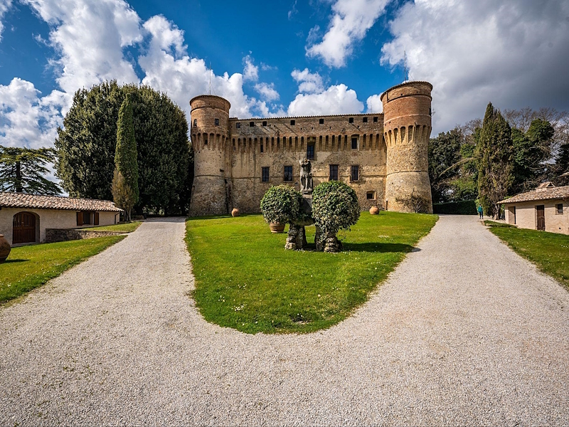 Civitella Ranieri Castle surrounded by greenery, with its entrance drive and circular towers.
