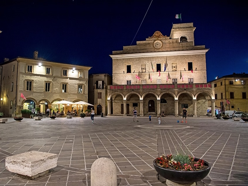 Piazza del Comune di Montefalco illuminata di sera con il Palazzo Comunale e i portici.