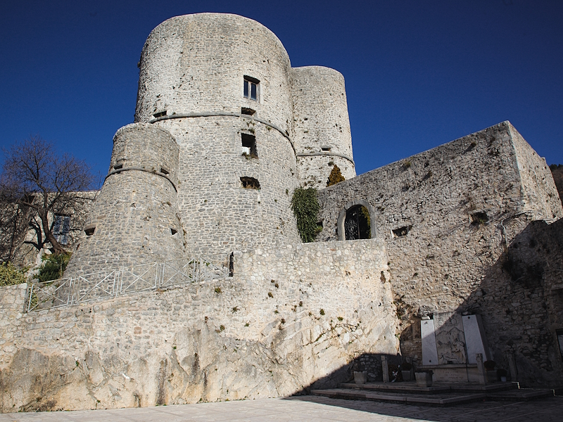 Festung von Polino mit zylindrischen Türmen und Steinmauern, von der Sonne beleuchtet unter blauem Himmel.