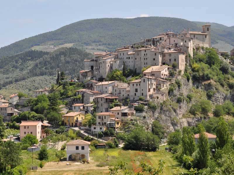 Panoramablick auf Casteldilago mit dem auf einer Anhöhe gelegenen Steindorf und den Bergen des Valnerina-Tals im Hintergrund.