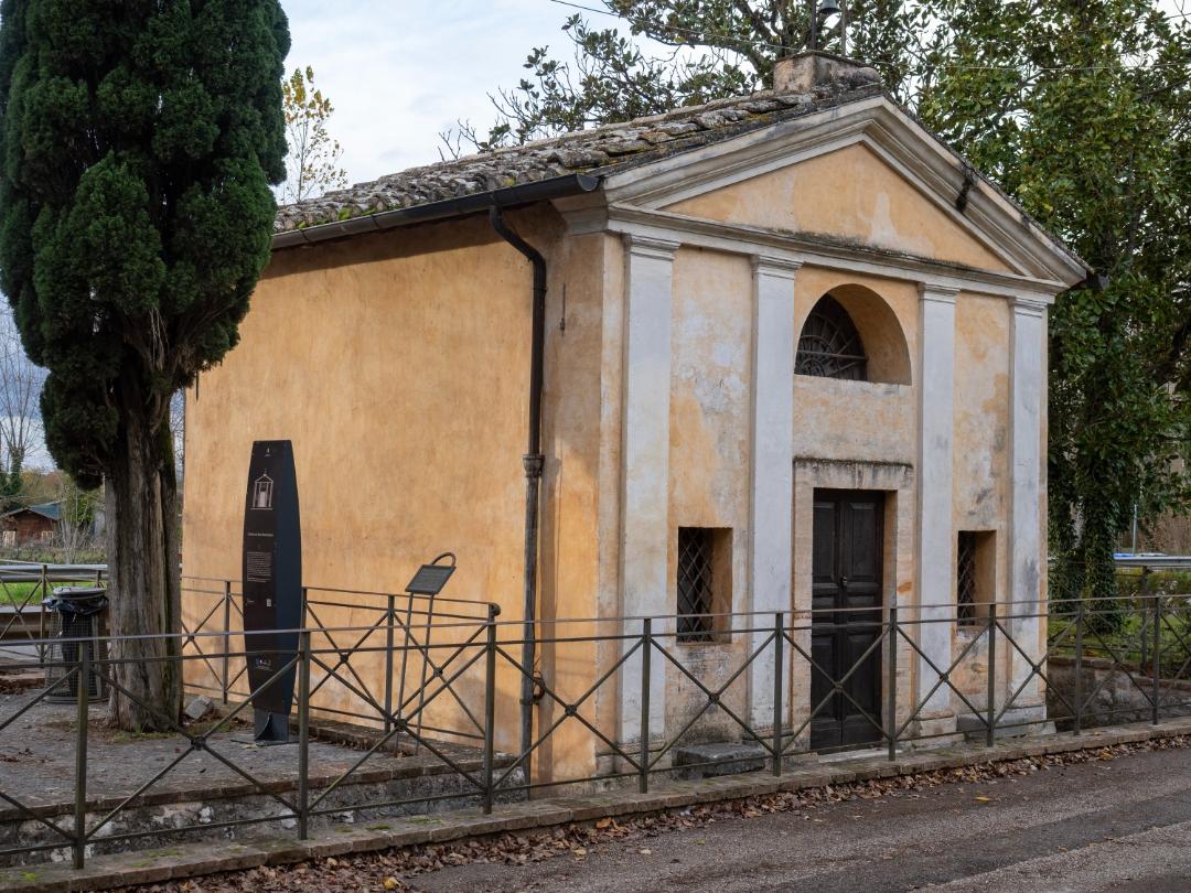 Exterior view of the Church of San Sebastiano, a small historic building with a simple façade and tiled roof, surrounded by trees