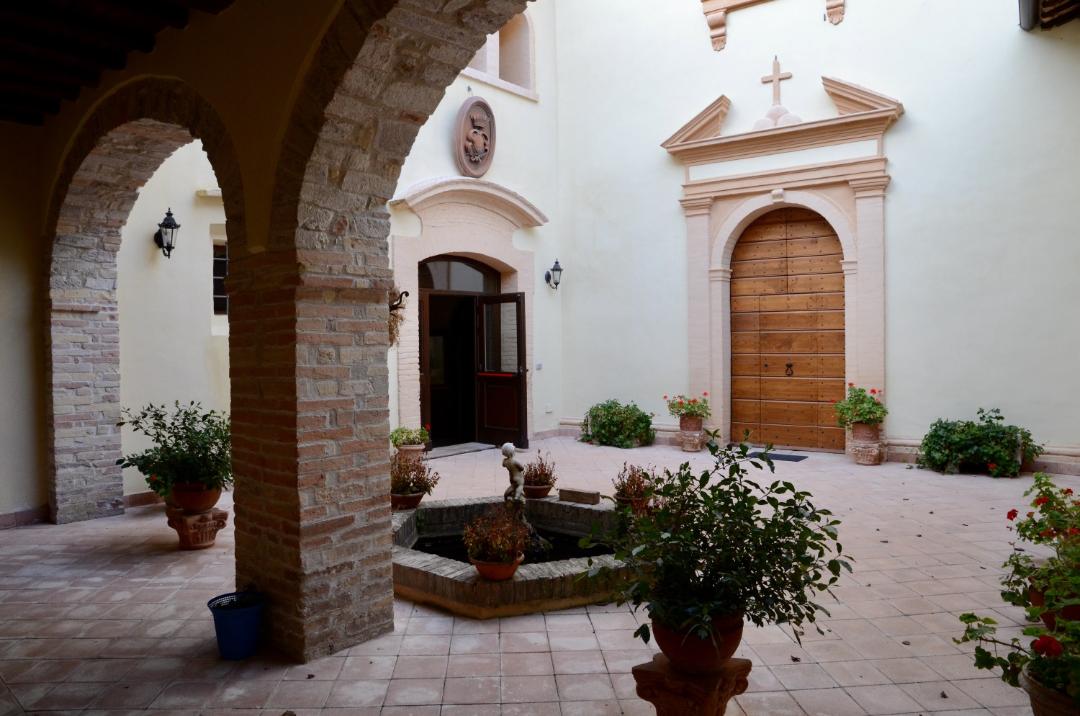 Chiostro con archi in pietra, cortile centrale con fontana e piante in vaso