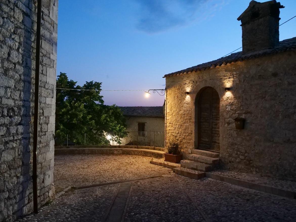 Campello Alto lit up at night, with medieval walls and stone houses overlooking the olive groves at the foot of the mountain