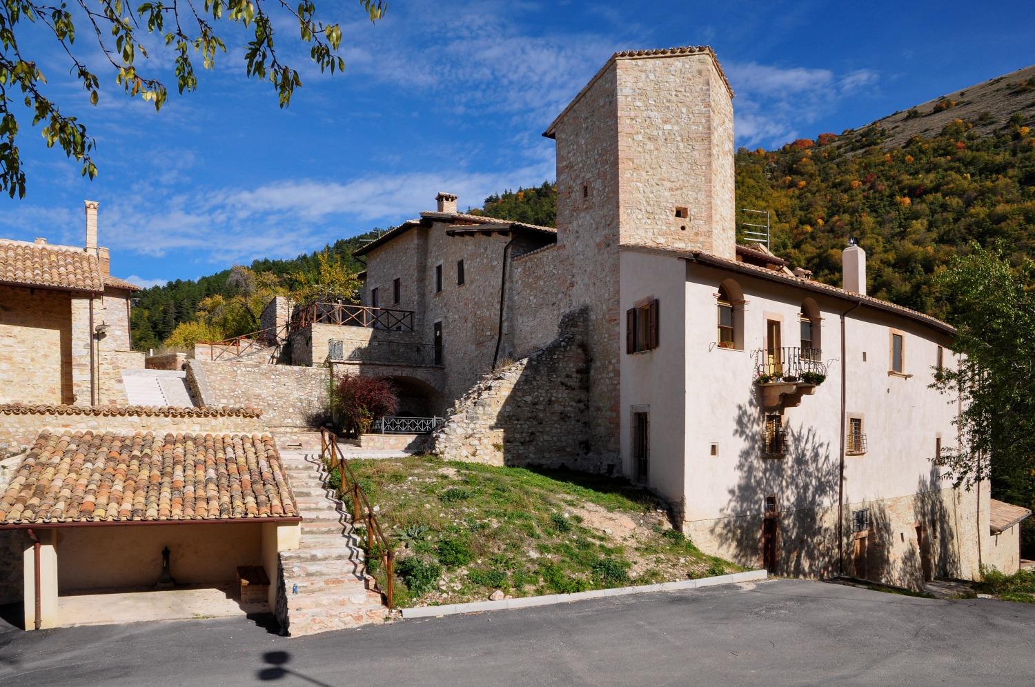 Stone houses and medieval tower of Acera on a wooded slope under a clear sky