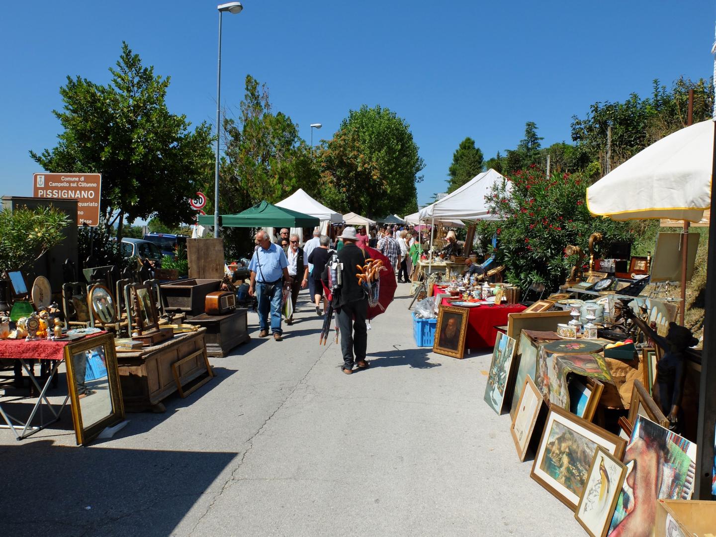 Stalls of an antique market with ceramics, vintage items and clothes displayed outdoors near the Fonti del Clitunno