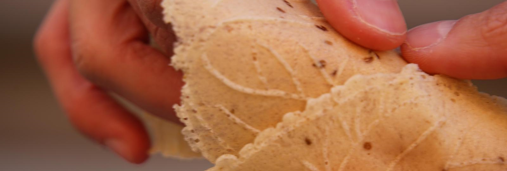 Hands holding a cone made from an artisanal wafer, with embossed patterns and anise seeds.