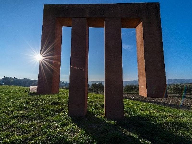 Monumental steel sculpture with geometric shapes installed on a hill in Brufa, with the Umbrian landscape in the background.