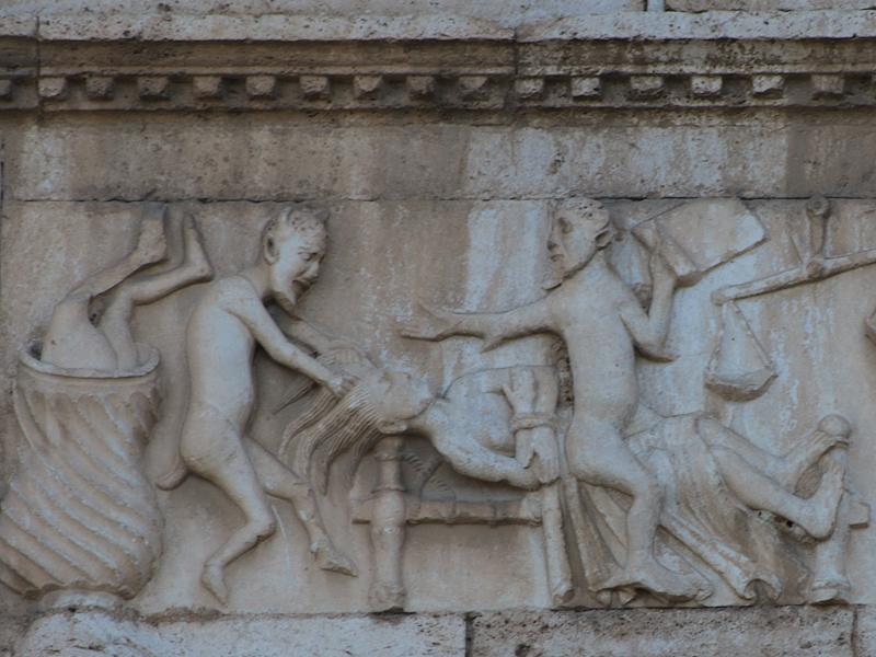 Rilievo medievale sulla facciata di San Pietro a Spoleto con figure demoniache che tormentano due personaggi.