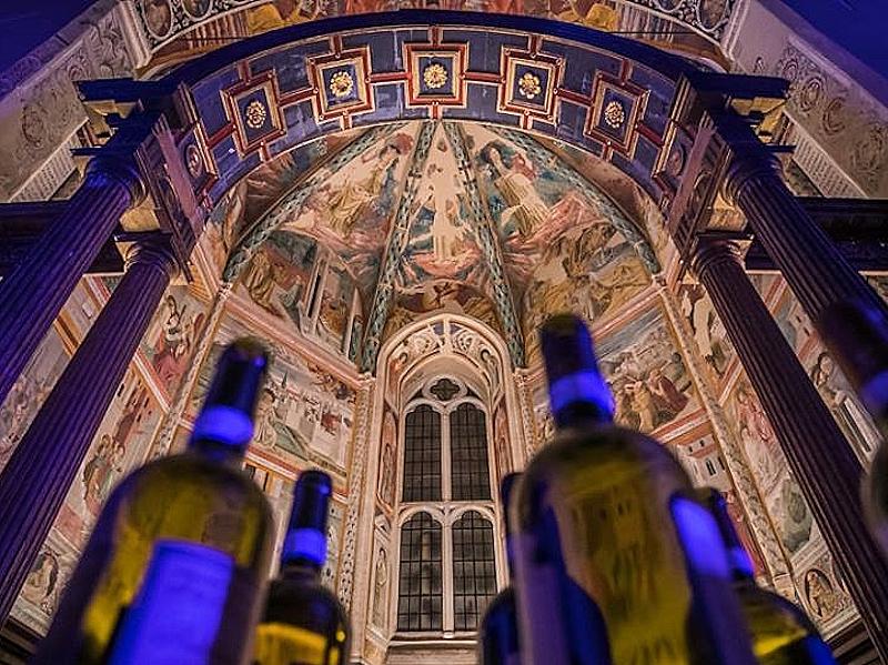 Wine bottles in the foreground inside a frescoed hall during the Enologica tasting event.