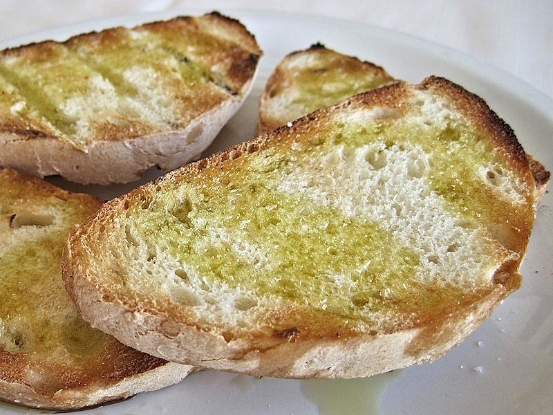 Slices of toasted bread seasoned with extra virgin olive oil served on a white plate.