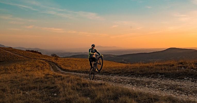 Cycliste sur un sentier vallonné au coucher du soleil en Ombrie, avec des paysages naturels et des montagnes en arrière-plan.