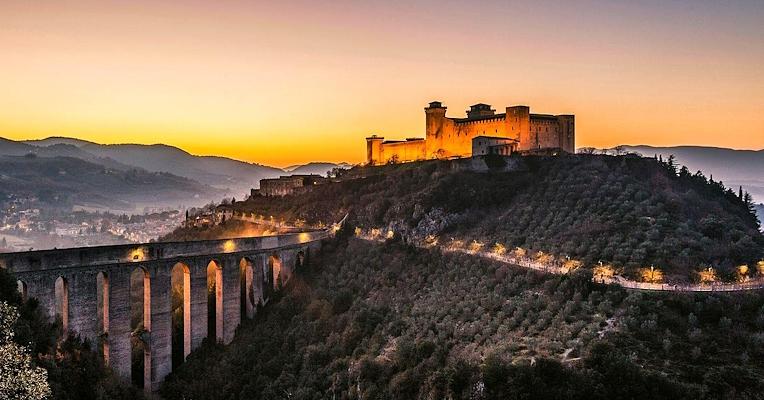 Panoramablick auf die Ponte delle Torri und die Rocca Albornoziana bei Sonnenuntergang über dem Tal und den Hügeln rund um Spoleto.