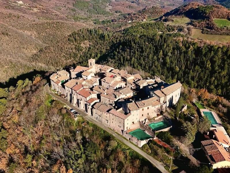 Vue aérienne du château médiéval de Macerino dans les Monts Martani, entouré de forêts ombriennes