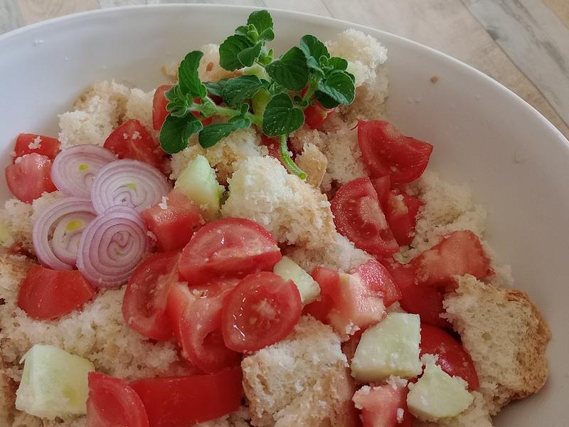 Bol blanc avec panzanella assaisonnée de tomates cerises, concombres et tranches d’oignon, garnie de menthe fraîche