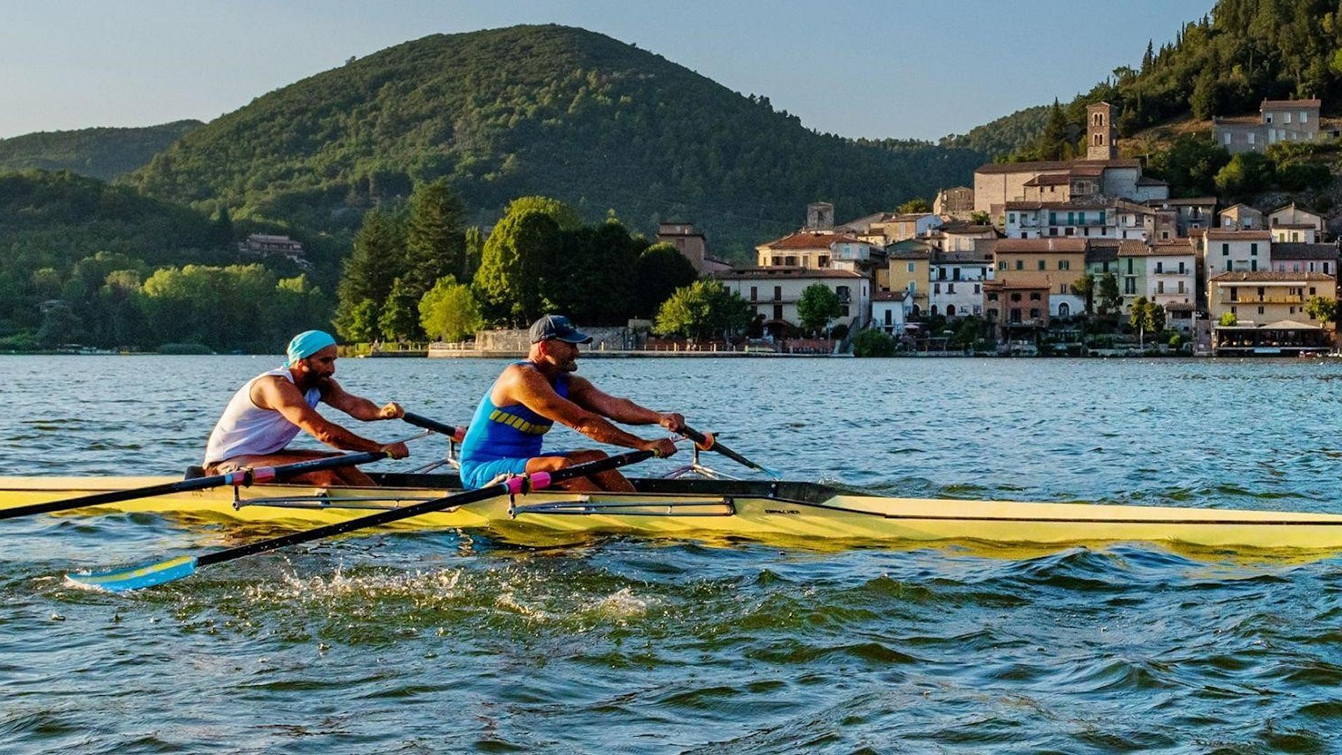 Deux rameurs sur le lac de Piediluco, avec le village au bord de l’eau et les collines en arrière-plan