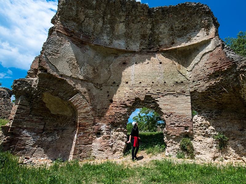 Ruins of the Roman Baths of Ocriculum with imposing brick walls and a person standing at the centre, highlighting the scale of the monument.